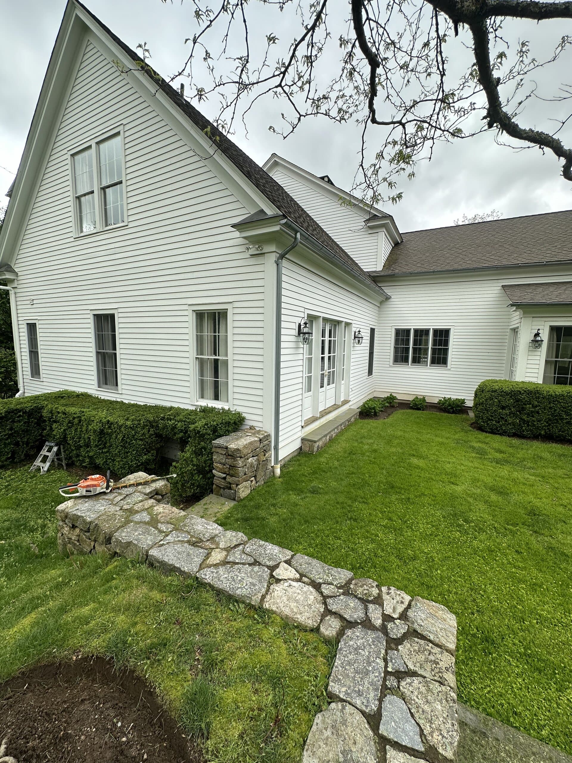 Dry-stacked stone wall beside a white colonial home