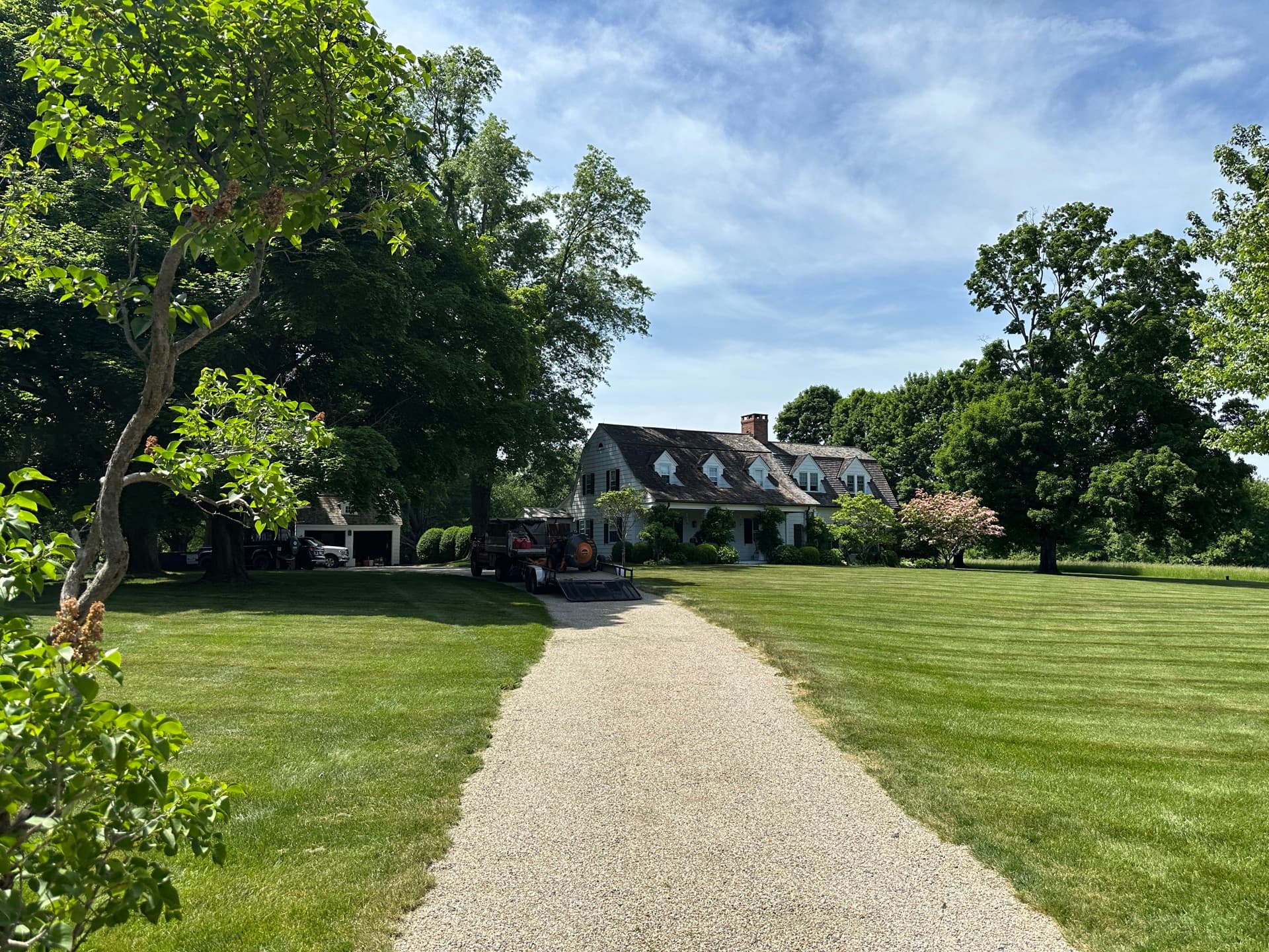 Manicured lawn and gravel driveway leading up to a Cape Cod home